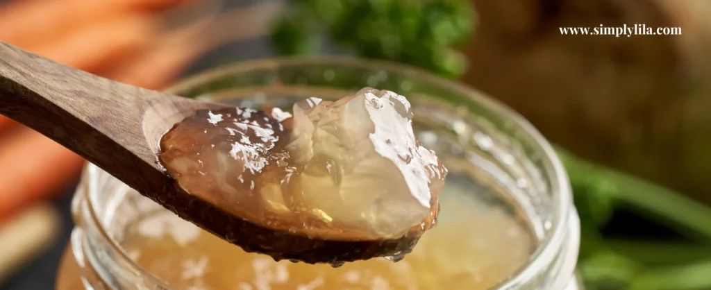 Wooden spoon lifting gelatinous bone broth from a glass jar with carrots and parsley in the background — fasting and refeeding nutrition