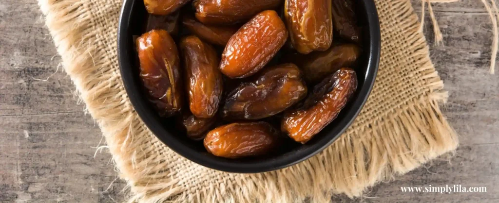 Bowl of glossy Medjool dates on rustic fabric and wooden surface