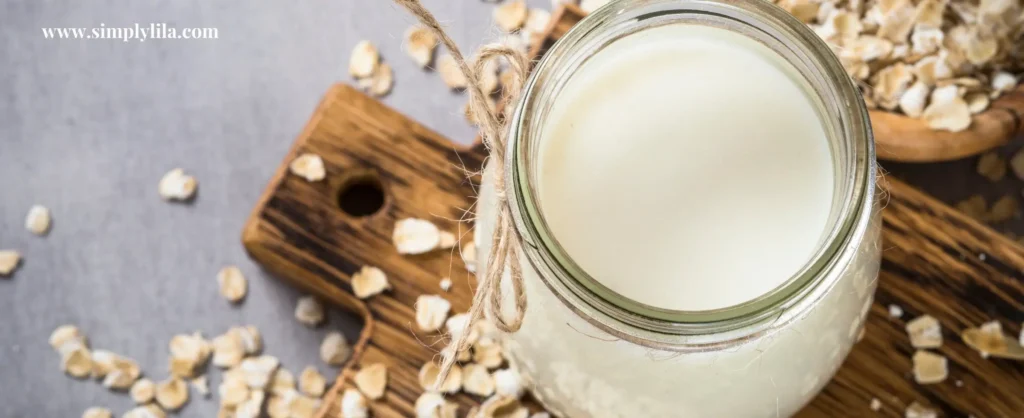 Jar of homemade oat milk on wooden board with scattered oats for natural oatmeal bath