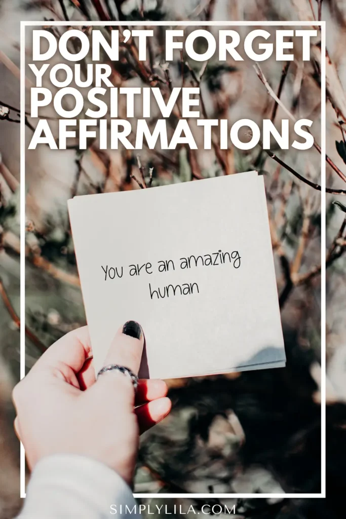 Hand holding a white card that reads “You are an amazing human,” with text overlay saying “Don’t forget your positive affirmations,” promoting the daily practice of self-affirmation for confidence and mental wellbeing.
