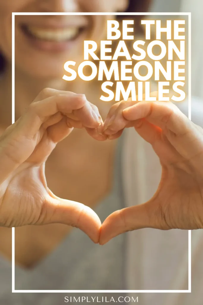 Close-up of a smiling woman forming a heart shape with her hands, with the text “Be the reason someone smiles,” symbolizing kindness, love, and spreading positivity.