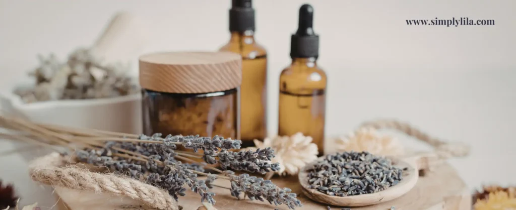 Two amber essential oil dropper bottles with dried lavender sprigs, wooden lidded jar and sola flowers on a warm natural surface