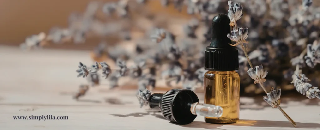 Two amber glass essential oil dropper bottles beside dried lavender sprigs on a rustic wooden surface