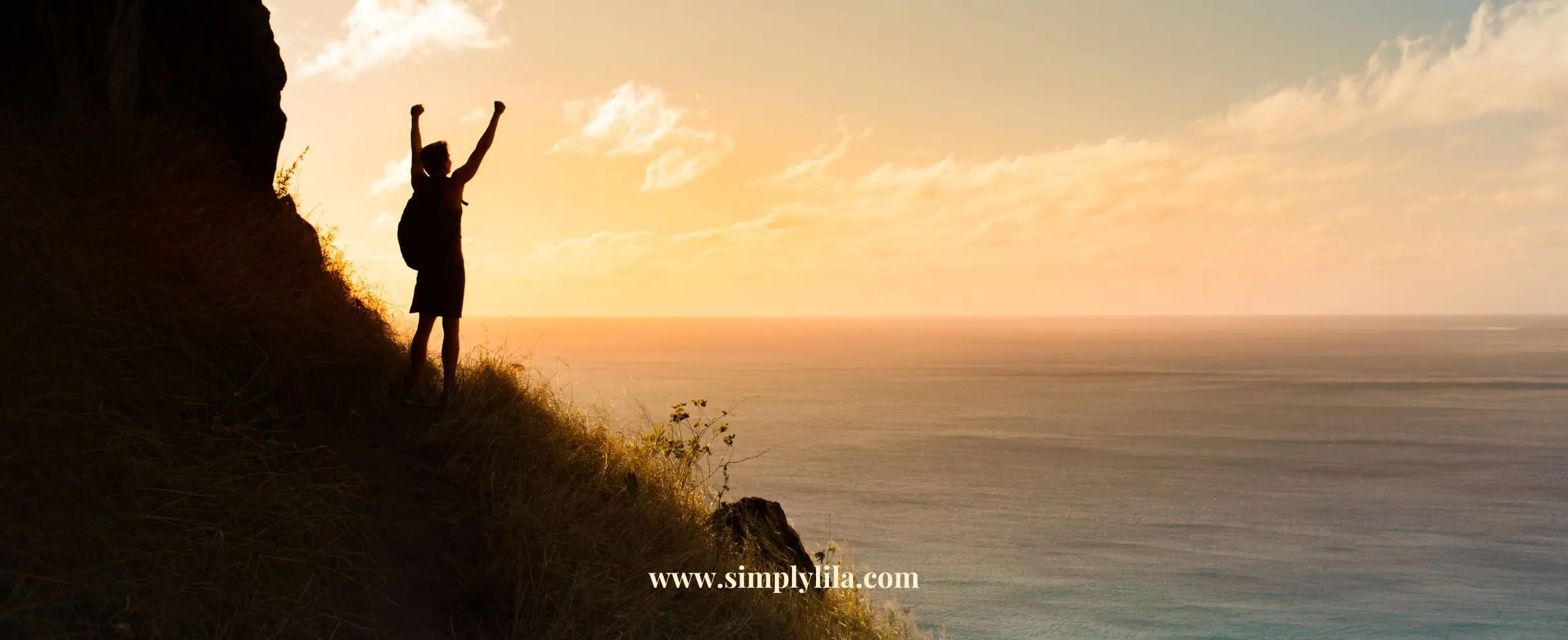 Person standing on cliff at sunrise with arms raised in victory