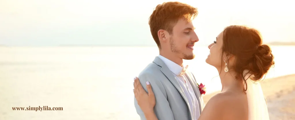 Bride and groom smiling at each other on a sunlit beach at their zero waste wedding