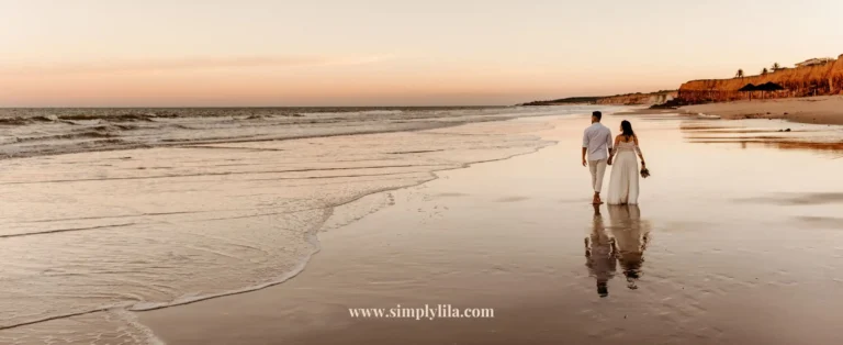 Bride and groom walking hand in hand along a sandy shoreline at sunset during their zero waste beach wedding