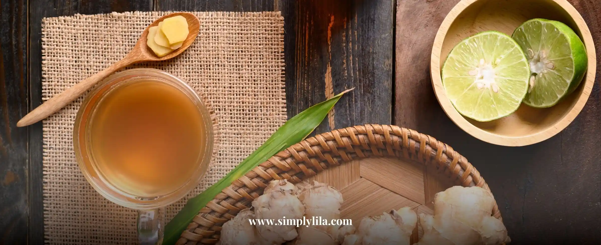 Cup of ginger and lime herbal tea with fresh ginger slices and halved lime on a rustic wooden table